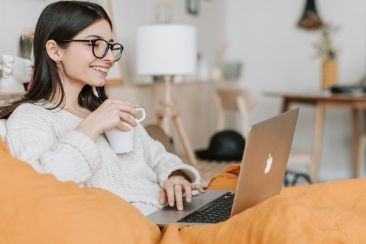 Kvinna med en kopp kaffe i handen framför sin laptop.